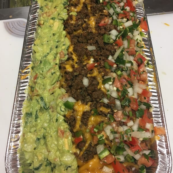 A catering tray of nachos with guacamole, ground beef, and pico de gallo.