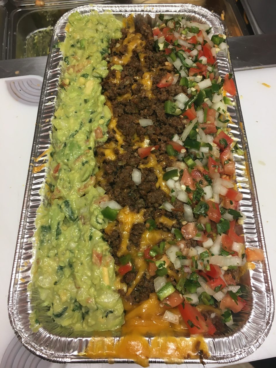 A catering tray of nachos with guacamole, ground beef, and pico de gallo.
