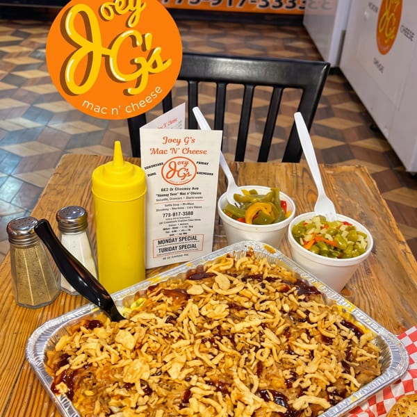 A large tray of mac and cheese with crispy onions and BBQ sauce, with sides of pickled vegetables.