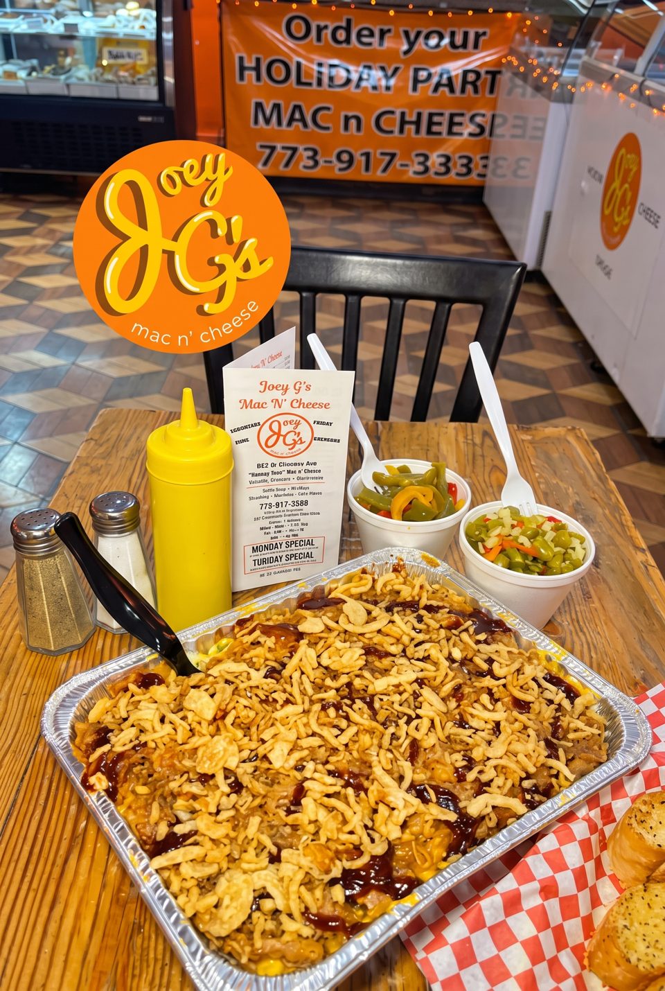 A large tray of mac and cheese with crispy onions and BBQ sauce, with sides of pickled vegetables.