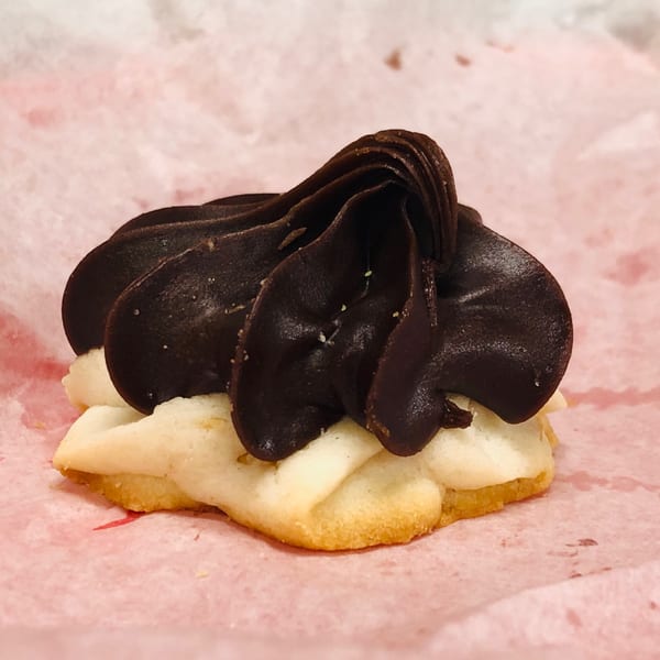 A shortbread cookie topped with dark chocolate frosting, resting on pink parchment paper.