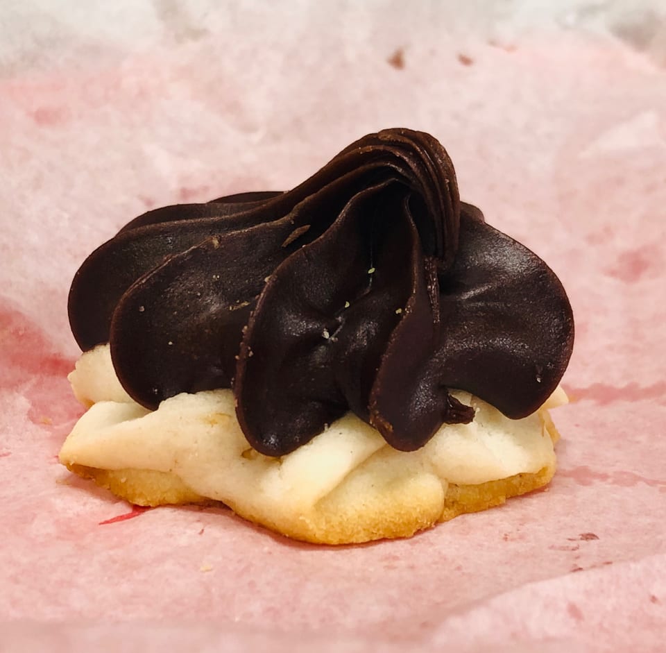 A shortbread cookie topped with dark chocolate frosting, resting on pink parchment paper.