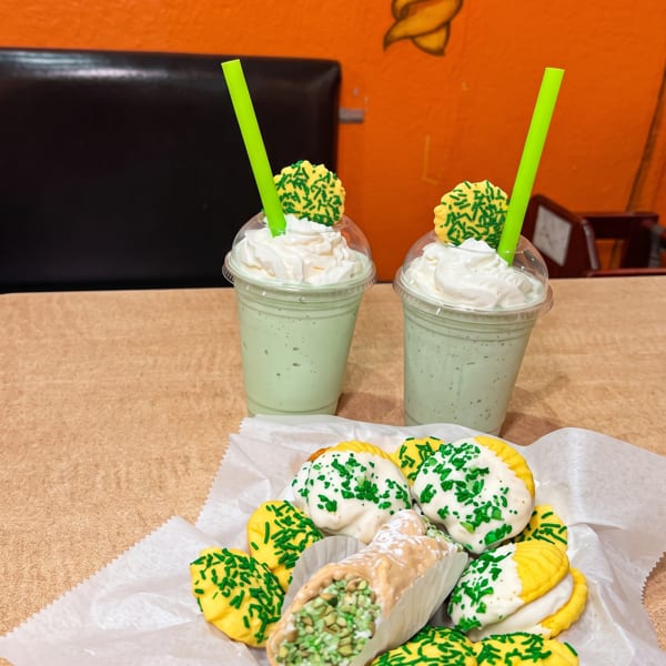 Two green milkshakes with whipped cream and cookies, alongside a cannoli and more cookies.