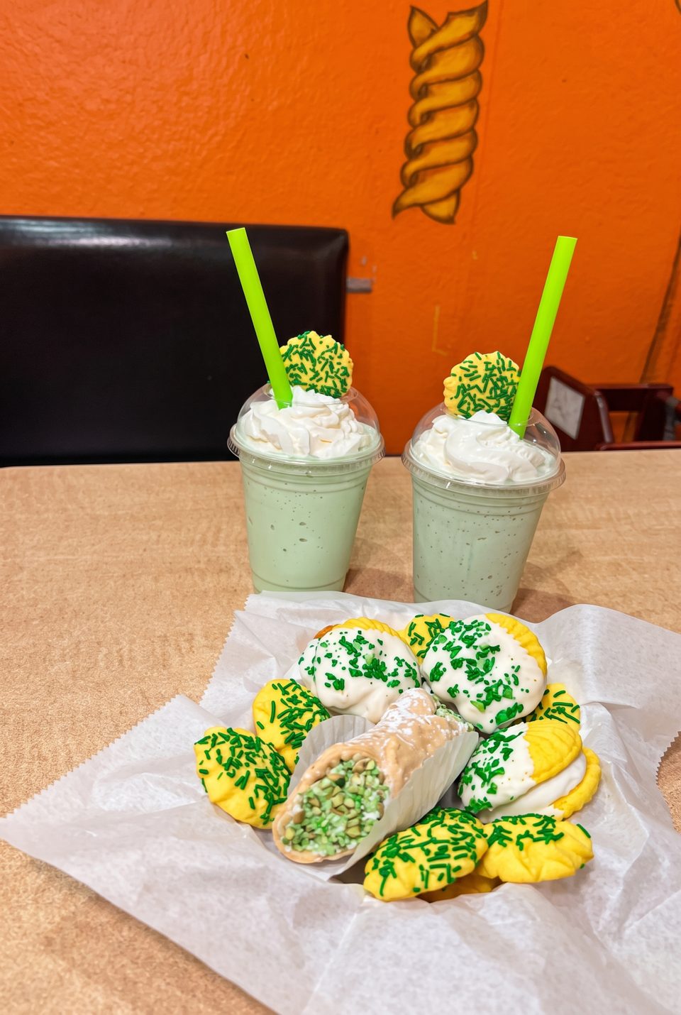Two green milkshakes with whipped cream and cookies, alongside a cannoli and more cookies.