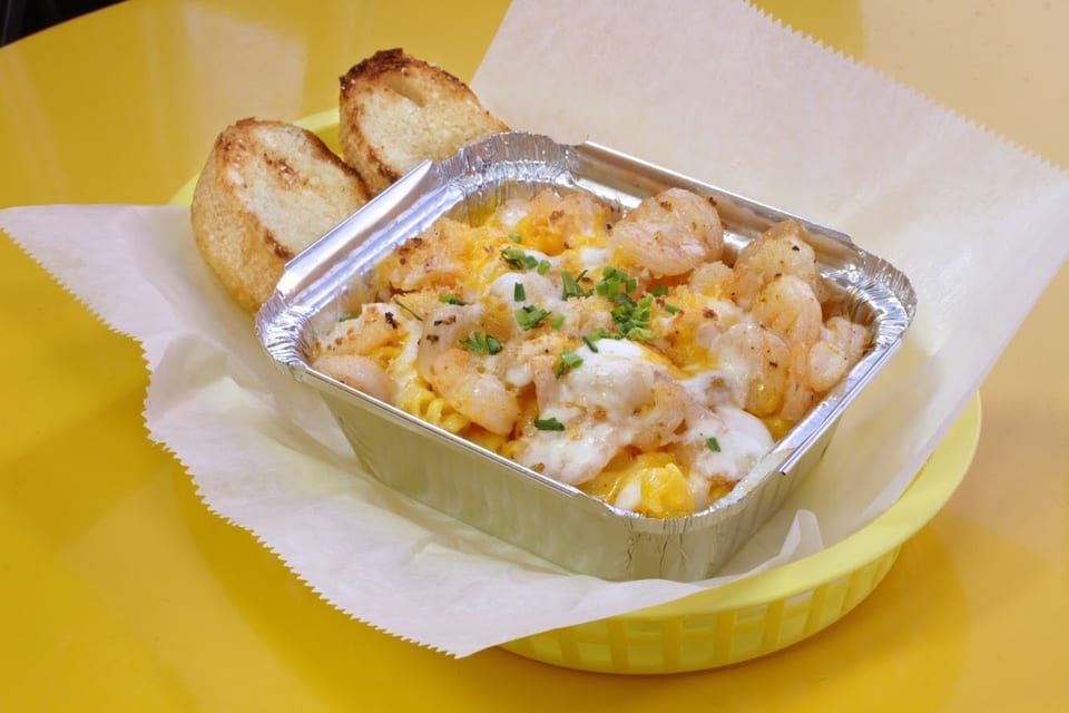 Shrimp mac and cheese in a foil container with two pieces of toasted bread.