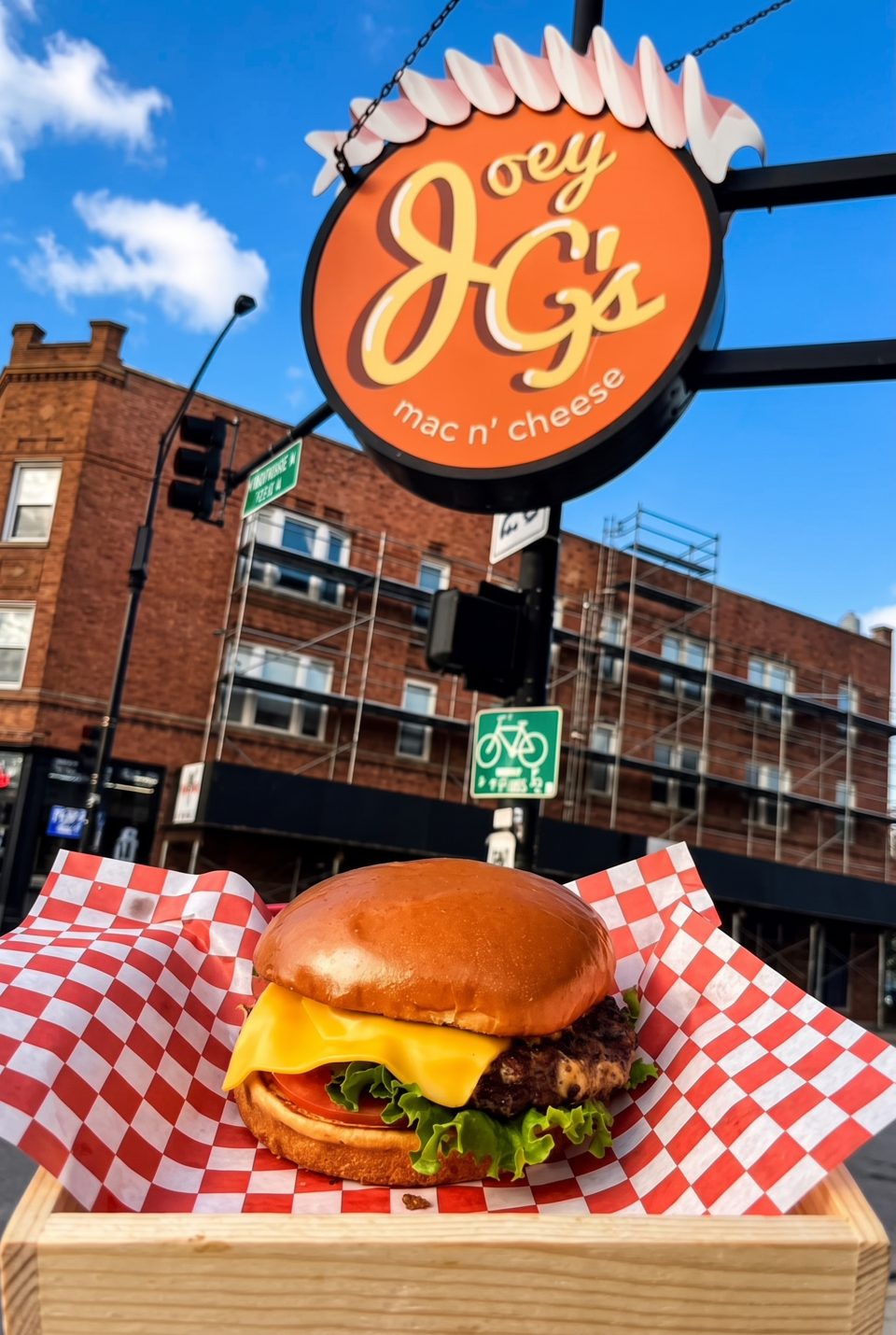 Cheeseburger in a red and white checkered wrapper, with the Joey G's Mac n' Cheese sign above.