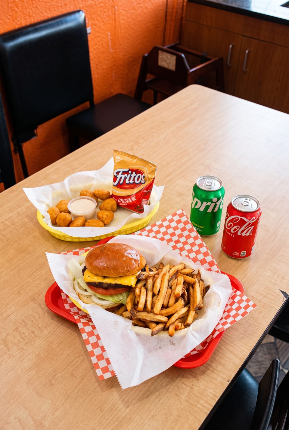 A burger and fries, chicken nuggets with Fritos, and two soda cans on a wooden table.