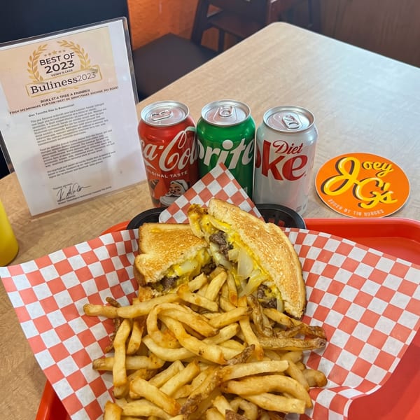 A grilled cheese burger and fries on a red tray with three soda cans and a "Best of 2023" award.