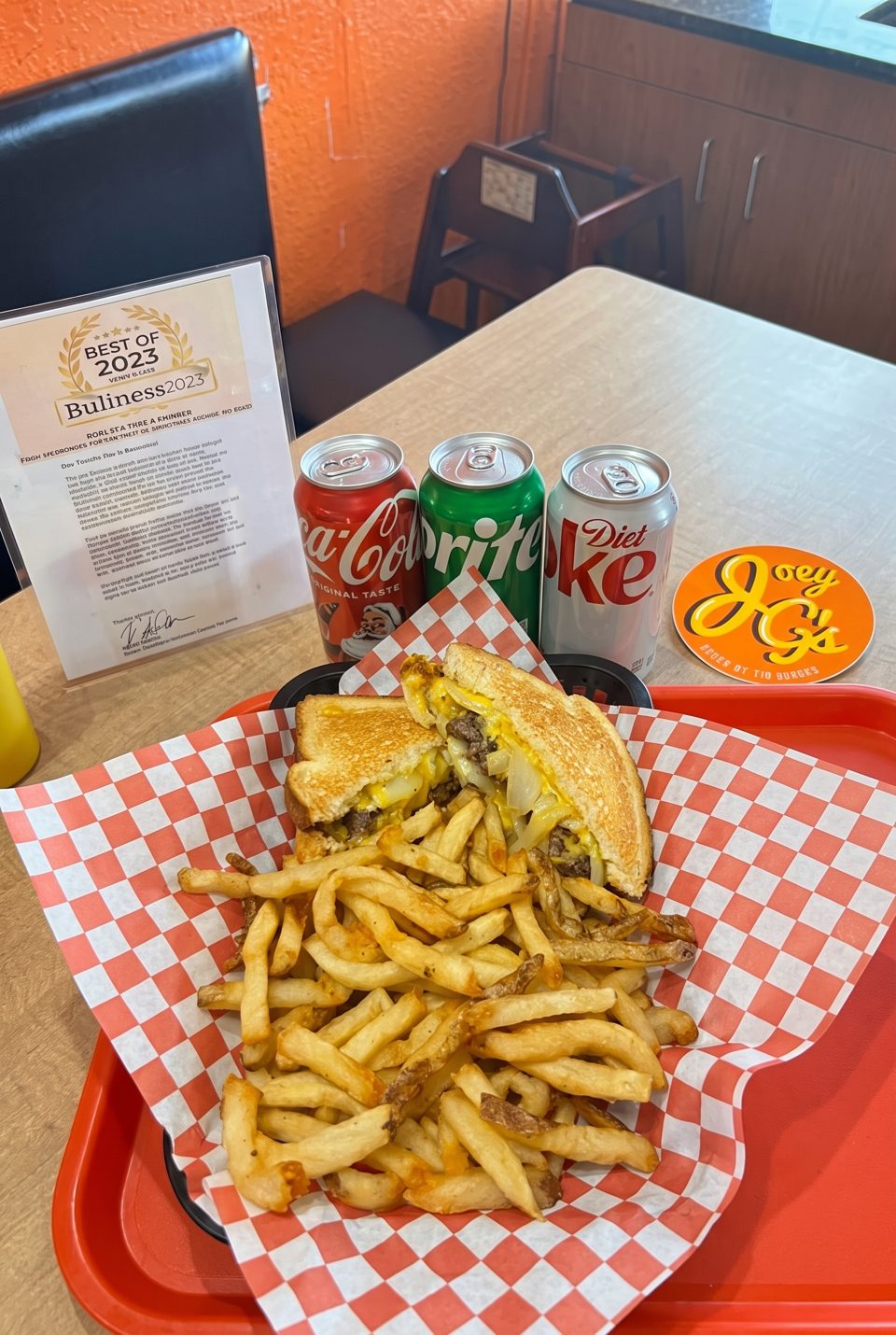 A grilled cheese burger and fries on a red tray with three soda cans and a "Best of 2023" award.