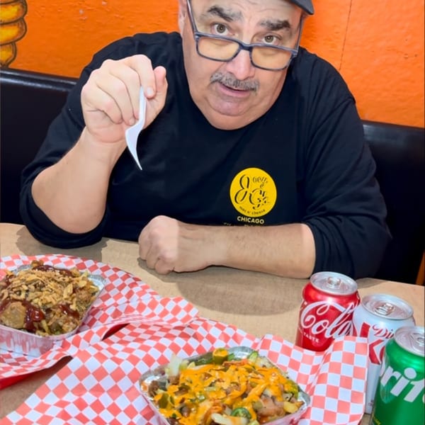 Man in a black hat and shirt with a yellow logo, holding a fork over two food trays.