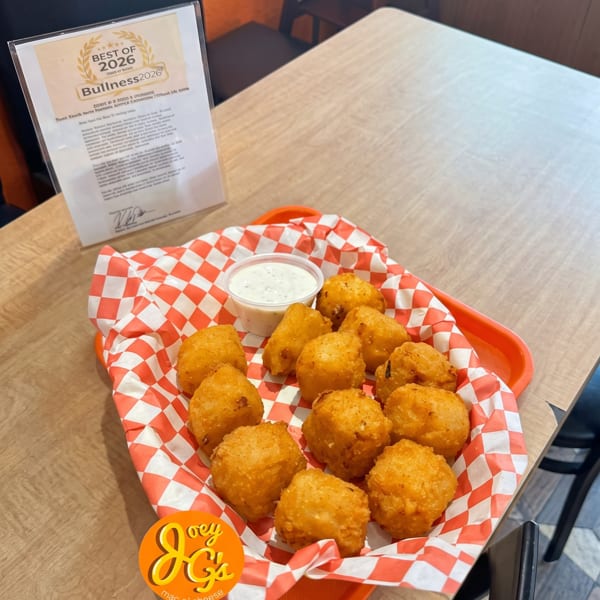 A basket of golden-brown fried mac and cheese bites with a side of ranch dressing on a wooden table.