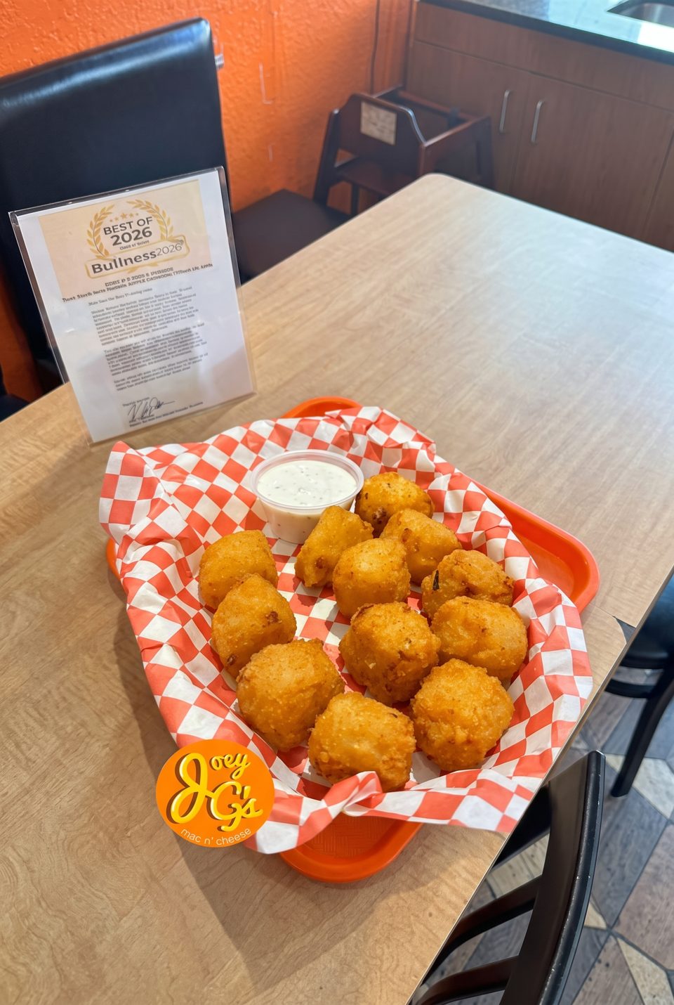 A basket of golden-brown fried mac and cheese bites with a side of ranch dressing on a wooden table.